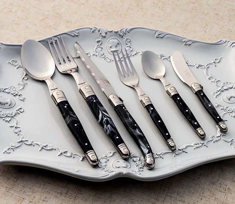 블랙 마블 패턴 핸들의 Laguiole Marble Cutlery Set가 문양이 있는 플레이트 위에 놓인 이미지 