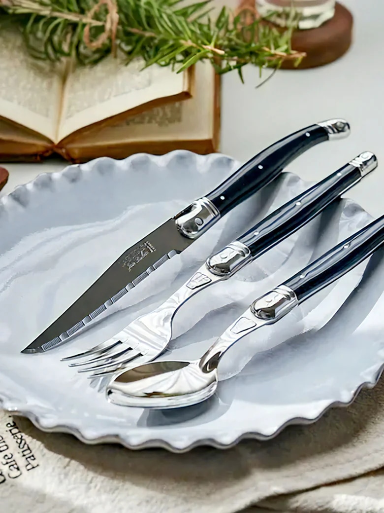 블랙 컬러 핸들의 Laguiole Cutlery Dinner Set가 화이트 플레이트와 함께 놓인 이미지 